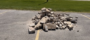 A pile of broken bricks lies on an asphalt surface next to a grassy area.